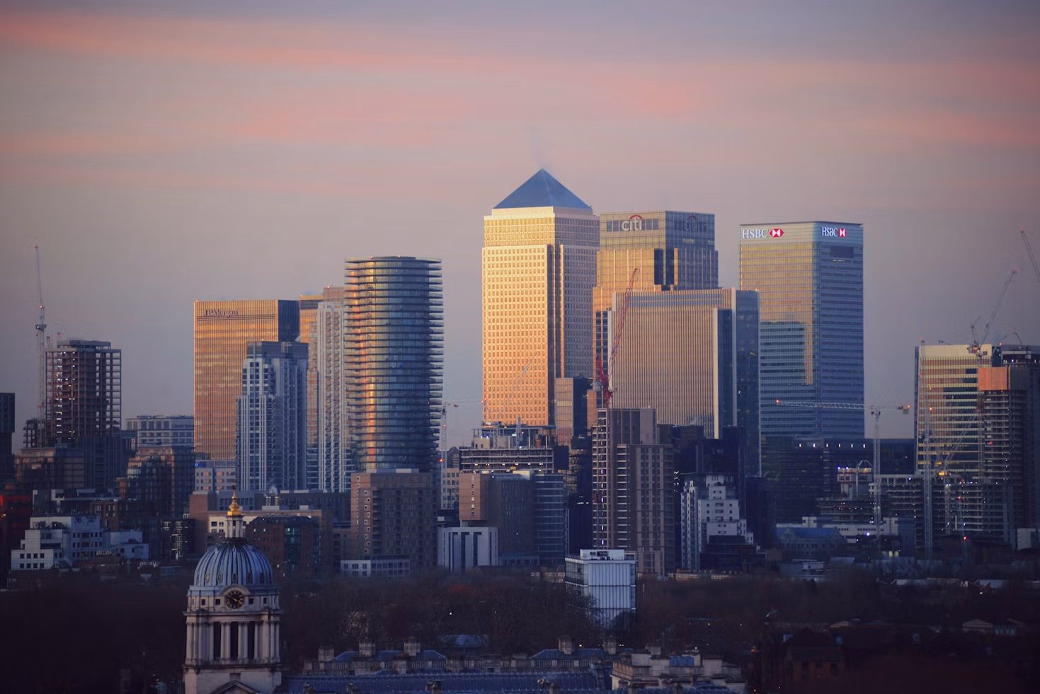 A professional looking out over the London skyline from a tower in Canary Wharf, the Thames and the City in the distance